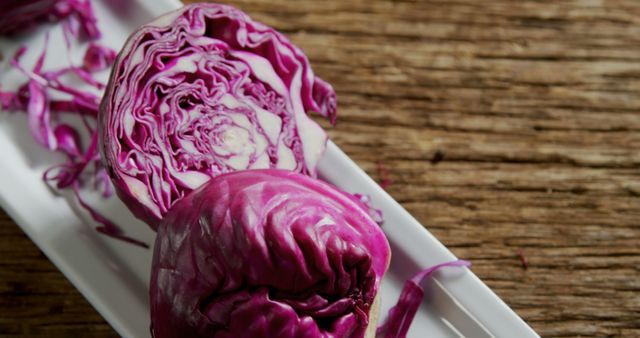 A sliced red cabbage rests on a white plate against a rustic wooden background, with copy space. Its vibrant purple hues and intricate patterns provide a natural aesthetic to the culinary presentation.