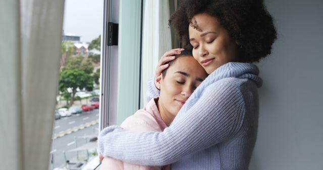 Two individuals are sharing a heartfelt hug by a sunlit window, showing empathy and emotional support. One person looks calm, while the other seems to find solace in the hug. It is a perfect representation of tenderness, friendship, and the deep emotional bonds we share with loved ones. Ideal for use in mental health awareness campaigns, friendship posters, or articles on emotional well-being and supportive relationships.