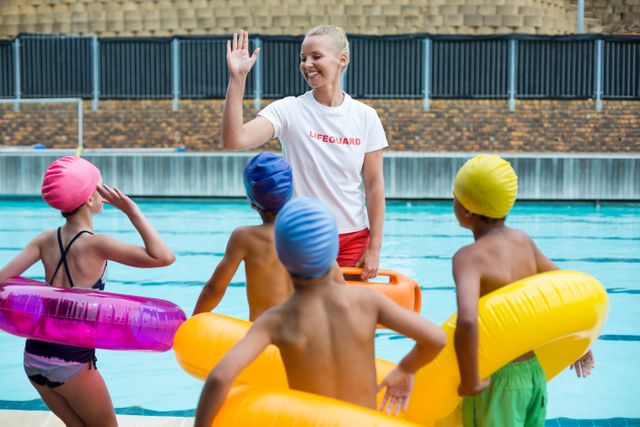 Cheerful lifeguard instructing children at poolside