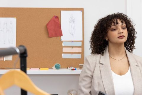 African american fashion designer checking phone reviewing corkboard and fabric swatches
