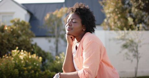 African american woman relaxing outdoors in coral shirt, wristwatch, serene contemplation
