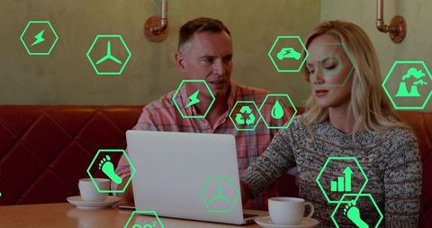 Professionals collaborating over laptop in coffeehouse discussing sustainability icons overlay