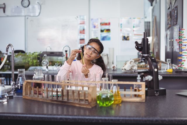 Young girl in science lab holding test tube, wearing safety goggles. Ideal for educational content, STEM promotion, school brochures, and science-related articles.