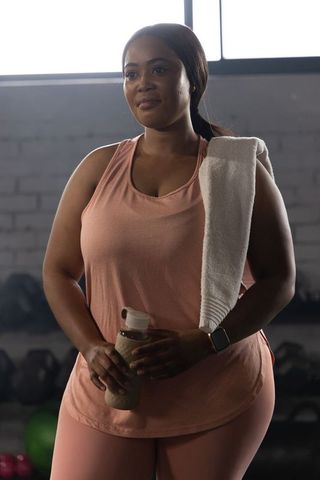African american woman wearing pink workout gear holding water bottle and towel in gym