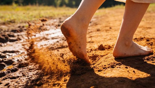 Bare feet kicking red dirt on rural trail with mud splash and sunlit motion