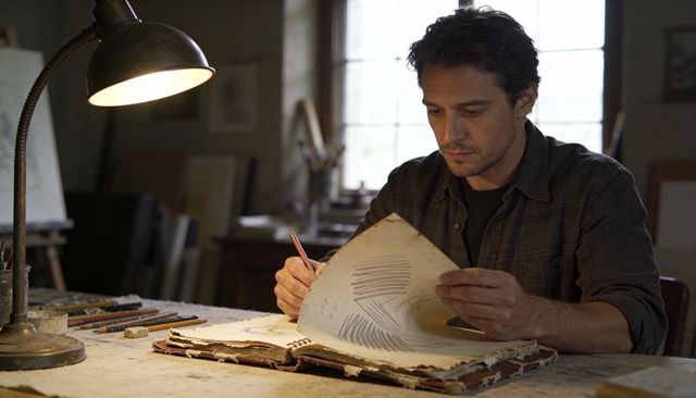 Artist turning sketchbook page in rustic studio studying pencil and charcoal drawings