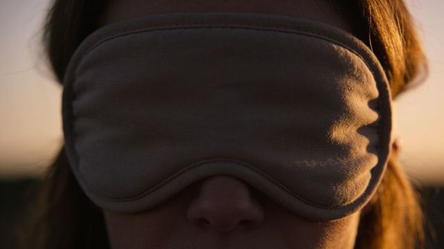 Woman wearing beige padded sleep mask at sunset with warm rim light, calm portrait