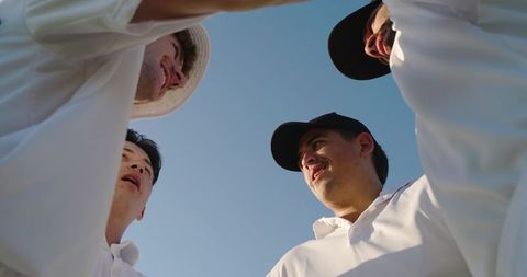 Multicultural teammates huddling under blue sky wearing white collared shirts and caps