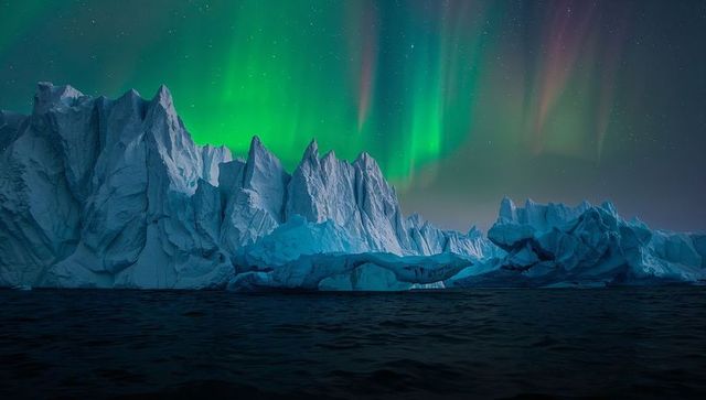 Northern lights above jagged iceberg ridge illuminating arctic frozen sea at night