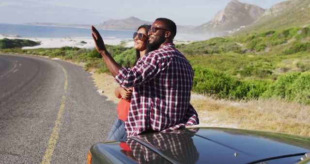 Couple embracing during a road trip at a scenic coastal viewpoint with mountains and ocean in the background. Perfect for illustrating travel, adventure, romantic getaways, and outdoor leisure activities. Suitable for travel blogs, tourism advertisements, and social media campaigns highlighting vacations and journeys.