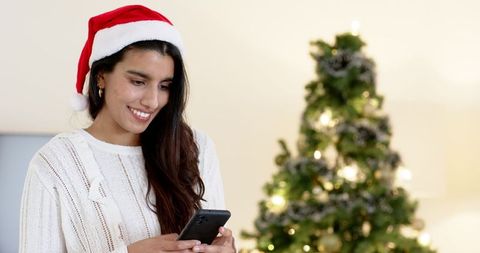 Celebrating Christmas: Indian Woman Smiling with Smartphone by Tree
