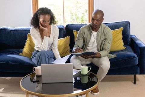 Black couple reviewing finances and planning at home, working with laptop and documents