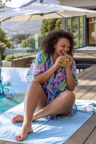 Sunlit resort relaxation: laughing woman sipping tropical drink by poolside