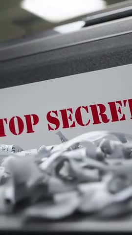 Vertical video panning over shred pile revealing red TOP SECRET text in office bin