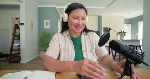 Senior asian woman podcasting from home studio wearing headphones adjusting microphone