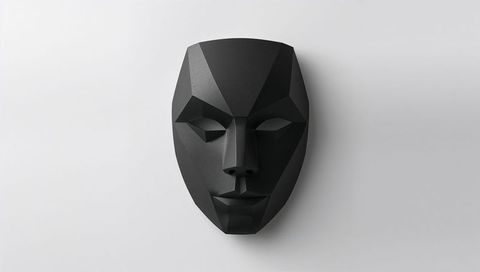 Matte black faceted geometric mask casting soft shadow on smooth light-gray wall minimal