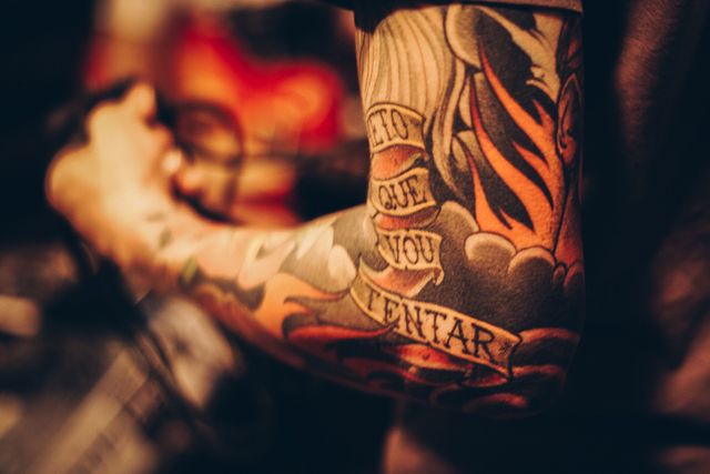 Close-up view focusing on a colorful tattoo sleeve wrapping around an arm. The tattoo features various vibrant elements and text. Ideal for use in articles or designs focusing on body art, tattoo culture, or artistic expressions.