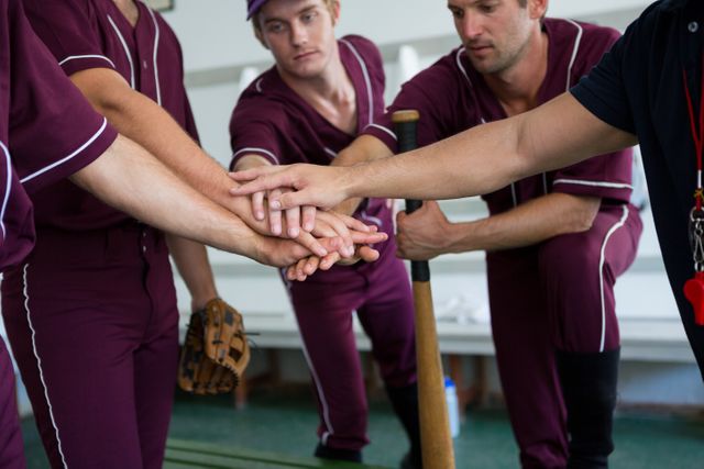 Baseball players in maroon uniforms are joining hands in a high five, showcasing teamwork and unity in a locker room. This image is ideal for promoting sportsmanship, team spirit, and athletic motivation. It can be used in sports-related articles, team-building advertisements, or motivational posters.