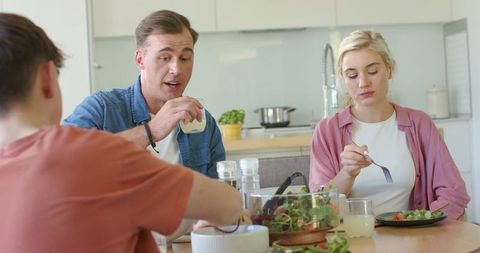 Family of three sharing healthy salad and conversation at modern kitchen dining table