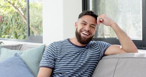 Bearded Man Laughing on Sofa in Modern Living Room