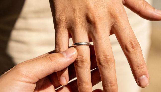 Sliding silver band onto finger during intimate ring exchange closeup with warm light