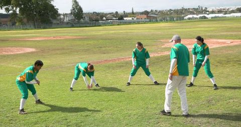 Softball team stretching warm-up with coach on field