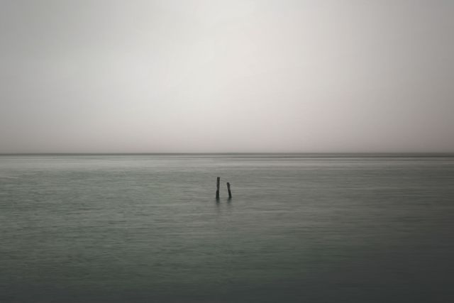 This depicts a calm seascape on a misty morning with a foggy horizon and tranquil waters. The minimalistic composition could be utilized in projects aiming to convey serenity, peace, or reflective moods. Ideal for backgrounds, meditation materials, or nature-themed marketing campaigns.
