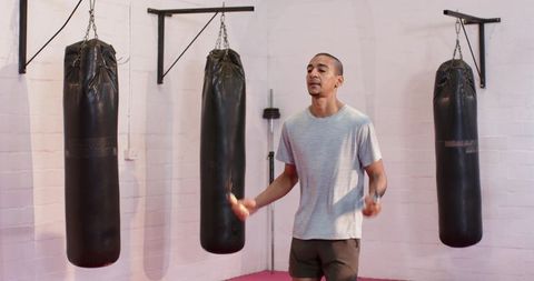 Young man skipping rope in boxing gym with three punching bags and barbell training