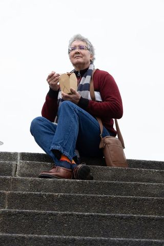 Senior man enjoying takeout noodles on outdoor concrete steps during cloudy urban day