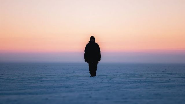 Walking solitary silhouette crossing frozen plain at twilight
