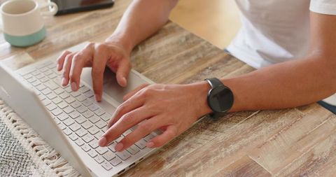 African american man typing on laptop at wooden table wearing smartwatch and coffee mug