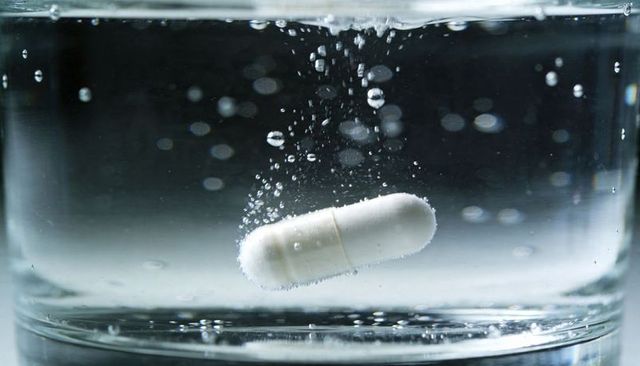 White capsule dissolving in water with rising bubbles and reflective glass base