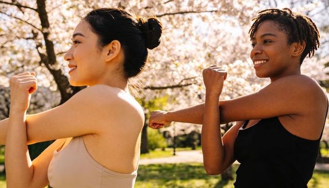 Two women stretching in spring park under blossoming cherry trees, outdoor fitness
