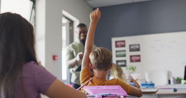 Image depicts young students actively participating in a classroom discussion, with one student raising a hand. Ideal for illustrating themes related to education, active learning, and student engagement in promotional materials, brochures, educational websites, or school newsletters.