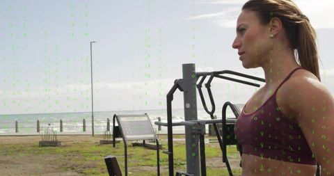 Athletic woman training at seaside outdoor gym wearing earbuds and maroon sports bra