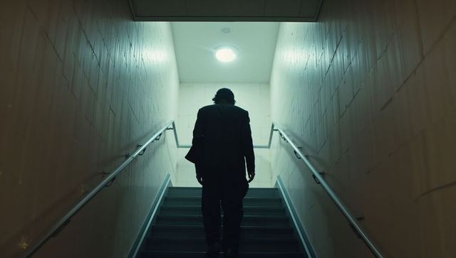 Lonely man climbing dim stairwell silhouetted by cold overhead light moody cinematic noir