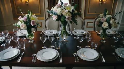 Camera gliding toward elegant dining table with three floral centerpieces and crystal glass