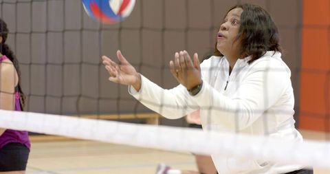 Female volleyball player reaching for red white blue ball at net during indoor gym action