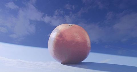 Glossy orange resting on white plane under vivid blue sky casting soft long shadow