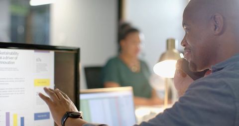 African American professional talking on phone pointing at monitor in open-plan office