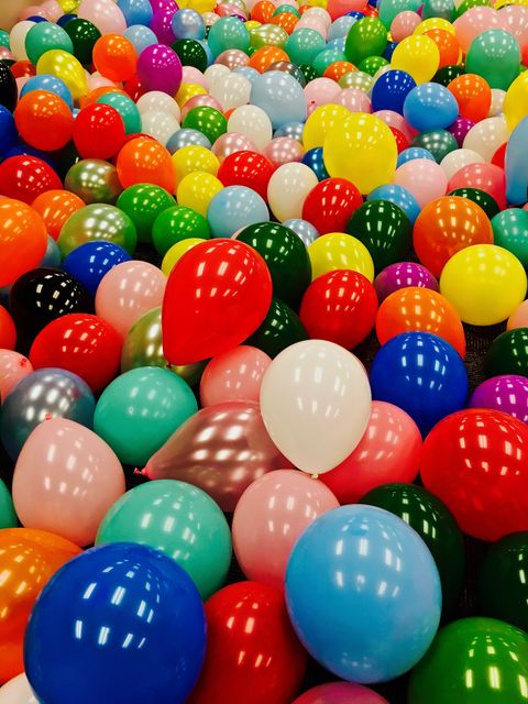 This image shows an array of colorful balloons covering a floor, creating a festive and lively atmosphere. Perfect for use in advertising children's parties, celebratory events, holiday promotions, and festive-themed invitations or digital banners.