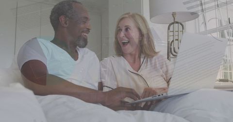 Happy Mature Couple Analyzing Financial Data on Laptop in Bed