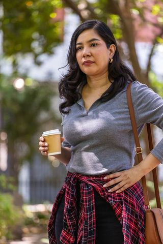 Urban woman holding takeaway coffee cup in park wearing casual fall outfit and plaid shirt