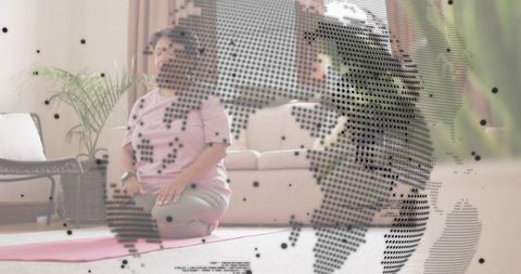 Senior woman kneeling meditating on pink yoga mat at home with digital globe overlay