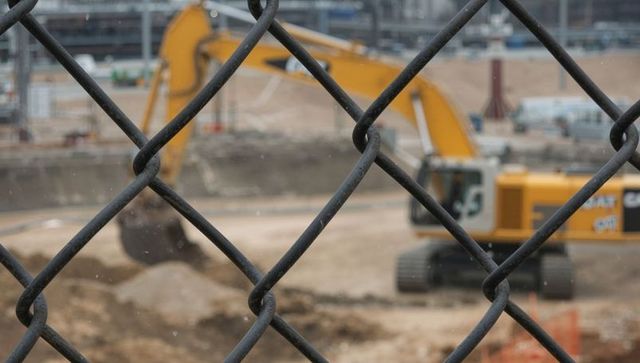 Chain-link fence framing yellow excavator at urban construction zone, safety barrier