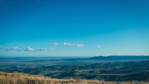 Golden hilltop overlooking rolling grassland and distant ridge under clear blue sky