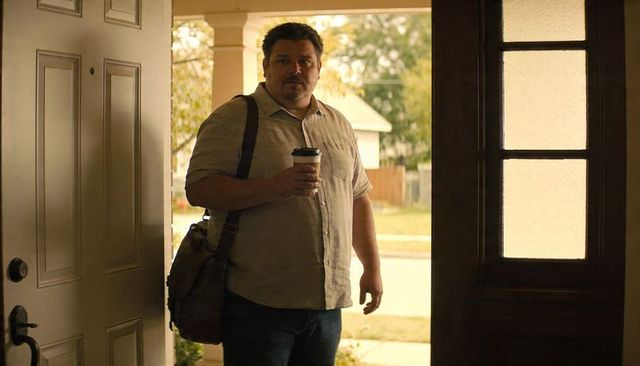 Middle age man standing at open door holding coffee cup and shoulder bag on porch morning