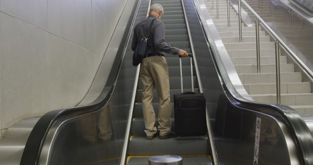 Depicts a senior man traveling with luggage, ascending an escalator in an airport terminal. Useful for themes of travel, retirement, adventure, and holiday trips. Could be used in travel agency promotions, airline advertisements, senior travel blogs, and airport informational guides.