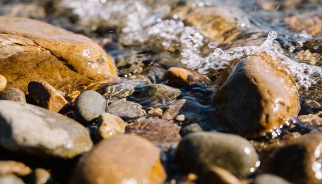 Macro close-up of clear water flowing over smooth pebbles and rounded rocks on coastline