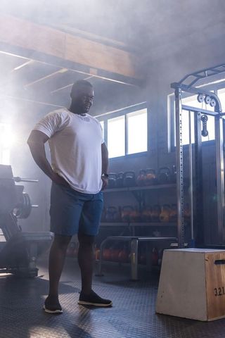 African-american man pausing mid-workout in industrial gym with hazy backlight for strength training
